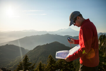 A man uses a compass and paper map to navigate while hiking in the North Cascade Mountain Range.