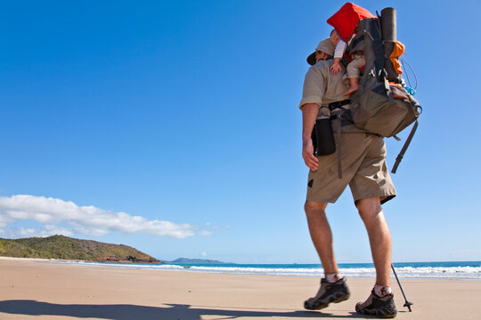 A man hikes while carrying his baby in Zoe Bay, Hinchinbrook Island, Queensland, Australia.