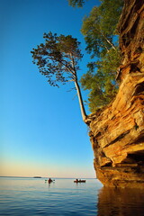 Kayaks paddle near sunlit cliffs at sunset.