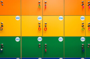 Orange, yellow and green lockers with keys and numbers in a public locker room in a children's entertainment center or in a clothing store. Warehouse in a supermarket.