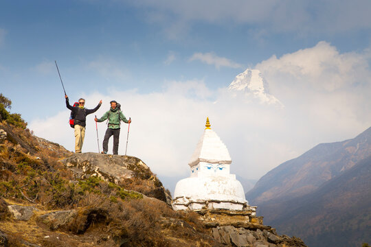 Two happy hikers near Buddhist Stupa with Ama Dablam mountain peak in background, Pheriche, Khumbu, Nepal