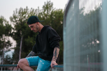 Man with tattoos in his arms is posing in a park