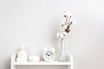 Alarm clock, vase, figurine and other details on white shelves. Minimalistic Scandinavian interior. Selecive focus, copy space