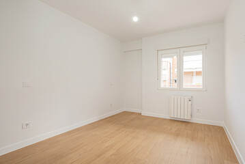 Fototapeta na wymiar Empty living room with laminated flooring and recently finished smooth white walls with an aluminum radiator under a window of the same material