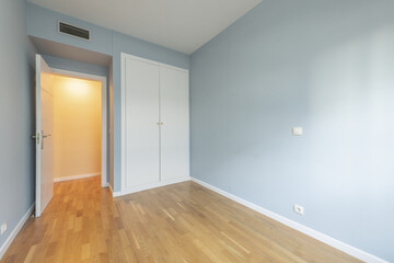 Fototapeta na wymiar Bedroom of an empty house with laminated oak flooring with a white built-in wardrobe, ducted air conditioning and white carpentry