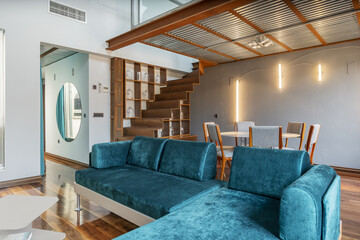 Living room of a loft-style house with a fireplace in a corner, an interior terrace, stairs with metal steps and a green velvet sofa, a metal ceiling and a circular mirror on the wall