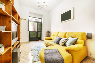 Living room of a rental house with a yellow sofa with a chaise longue, a wooden shelf and access to...