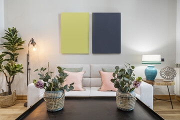 Living room of a house with artificial floral decorative elements and a white two-seater sofa with cushions