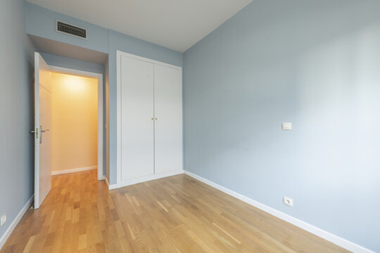 Bedroom of an empty house with laminated oak flooring with a white built-in wardrobe, ducted air conditioning and white carpentry