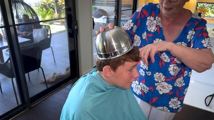 A boy nervously lets his grandmother use a bowl to help cut his hair