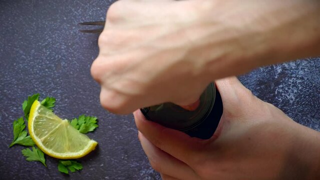 Hand opening a can of octopus on a dark blue table with lemon and parsley. Ready to eat.