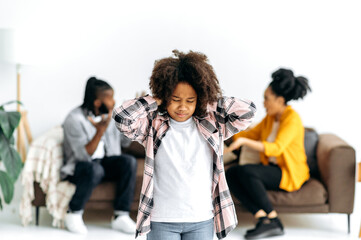 Difficulties in the family, conflict. An African American unhappy preschool girl closed eyes and ears, against the background, parents sort things out, shout at each other, swear, the child is scared