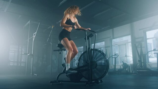 Side view of active, sporty woman using an elliptical machine. Blonde-haired, caucasian female athlete working out in modern gym studio alone. High quality 4k footage