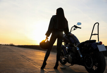 Woman with helmet near motorcycle at sunset, back view