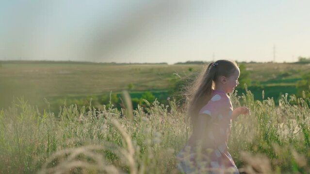Kid runs across meadow. Happy running child in field. Happy family. Little happy girl runs on grass, smiles, in slow motion. Childhood dream concept. Cheerful little girl playing in park in summer.