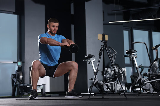 Trainer streaming online workout with phone at gym