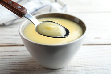 Bowl and spoon of Ghee butter on white wooden table, closeup