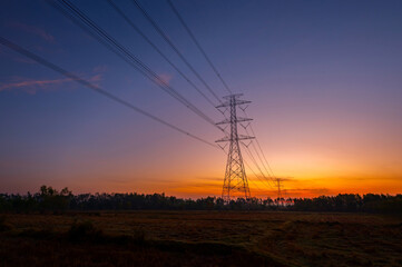 Silhouette electric pole and high voltage tower.High voltage transmission pole against morning sun in rice fields background.