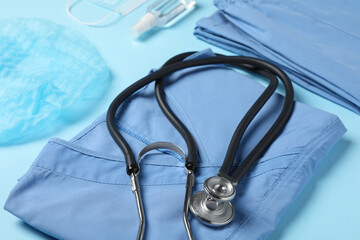 Medical uniform, stethoscope and antiseptic on light blue background, closeup view