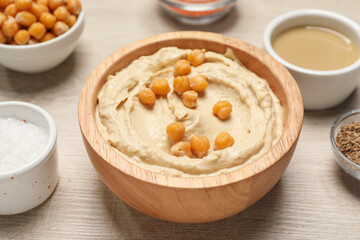 Obraz na płótnie Canvas Bowl with delicious hummus and chickpeas on light wooden table, closeup