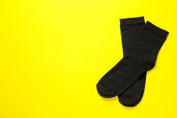 Pair of black socks on yellow background, flat lay. Space for text