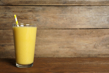 Glass of tasty smoothie with straw on wooden table. Space for text