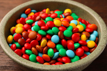 Bowl with tasty colorful candies on wooden table, closeup