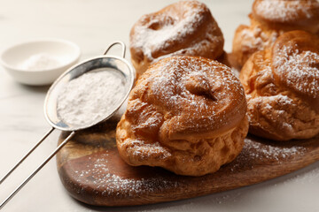 Delicious profiteroles with powdered sugar on wooden board, closeup