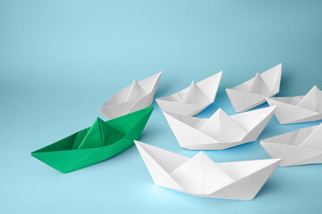 Group of paper boats following green one on light blue background. Leadership concept