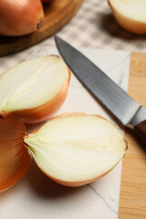 Whole and cut onions with knife on table, closeup