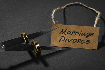 Scissors with wedding rings on blades and paper card Marriage Divorce against black background,...