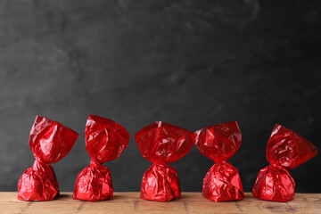 Delicious chocolate candies in red wrappers on wooden table
