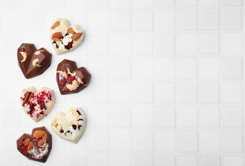 Tasty chocolate heart shaped candies with nuts on white tiled table, flat lay. Space for text