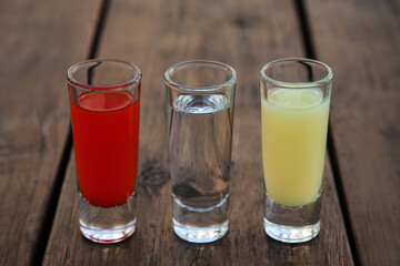Shots with lime juice, tequila and sangria as colors of mexican flag on wooden table, closeup. Traditional serving