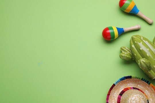 Colorful maracas, toy cactus and sombrero hat on light green background, flat lay with space for text. Musical instrument