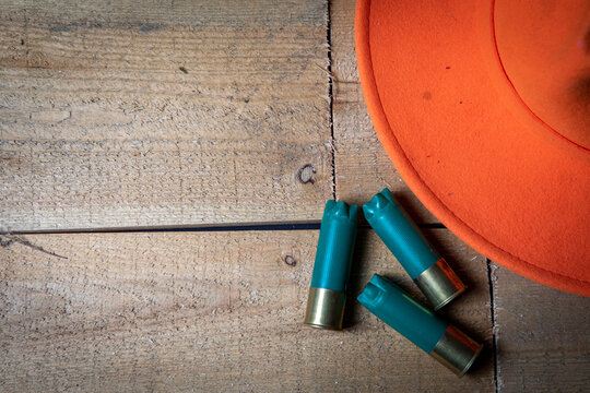 Three green shotgun shells and a orange hunting hat on a wooden background