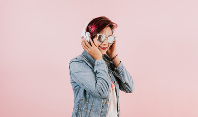 young hispanic woman girl listening music with headphones  and holding mobile phone on coral pink background with copy space studio portrait in Mexico Latin America