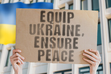 The phrase " Equip Ukraine, Ensure Peace " is on a banner in men's hands with blurred background. Stability. National. Unity. Equipment. Conflict. Agreement. Resilience. Safety. Strength. Strategic
