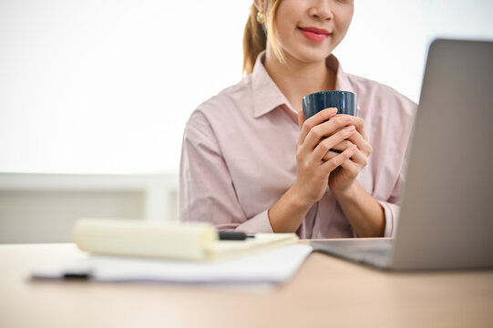 cropped image, Asian businesswoman holding a cup of coffee while working at her office desk.