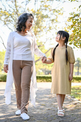Lovely Asian grandmother and granddaughter holding hands, walking along in the park