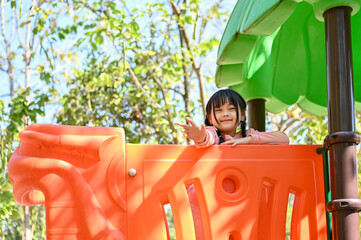 Cute and adorable Asian girl playing on playground equipment, having fun time in the park