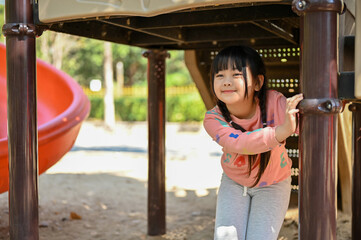 Cute Asian girl enjoys playing on outdoor park playground on the weekend, or school yard
