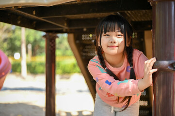 An adorable Asian girl having fun time, playing on playground in the city park on the weekend.
