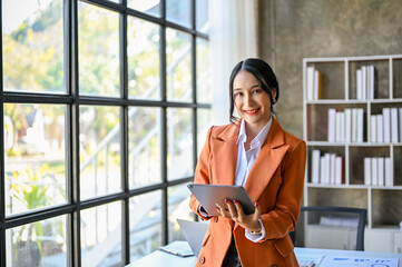 Attractive Asian businesswoman or female CEO stands in her office with digital tablet