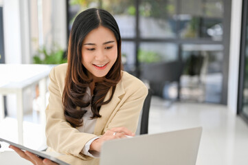 Fototapeta na wymiar Beautiful Asian businesswoman looking at laptop screen, working on her business tasks on laptop.