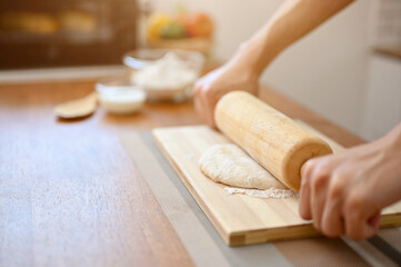 close-up image of a male baker kneading dough with a rolling pin on kitchen table