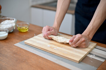 Close-up hand image of a male baker kneading raw dough, making homemade pastry at home.