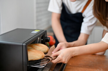 Close-up image, Asian couple putting tray in the oven, enjoy baking in the kitchen together