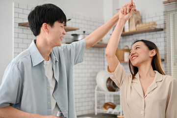 Loving and playful Asian couple dancing in the kitchen while preparing breakfast.