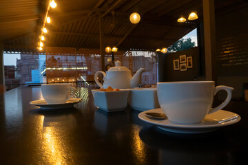 Beautiful interior view of restaurant at Jodhpur, Rajasthan, India. White cups, dishes and tea pot with reflection of decorated lights on shining table top.